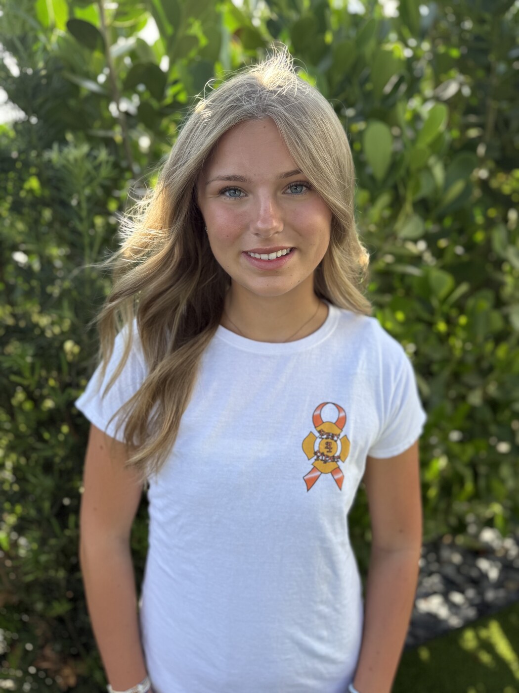 Piper, founder of Piper's K.I.D.S., wearing a white tee with the foundation's ribbon